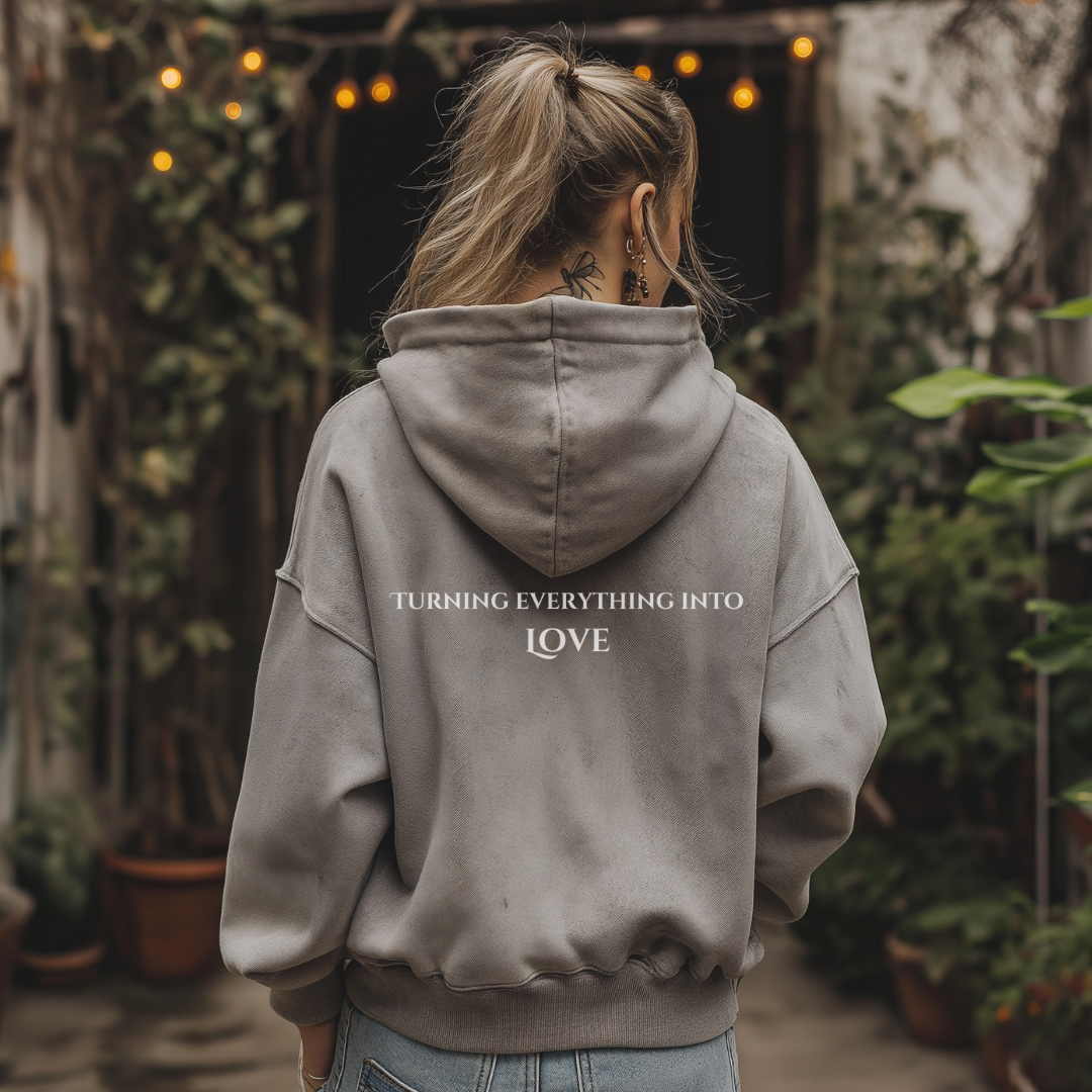 Model wearing hoodie that reads ALCHEMIST in distressed block letters across the chest. "Turning Everything Into Love" in two lines of smaller block letters is written on the back.
Embody love in all things.