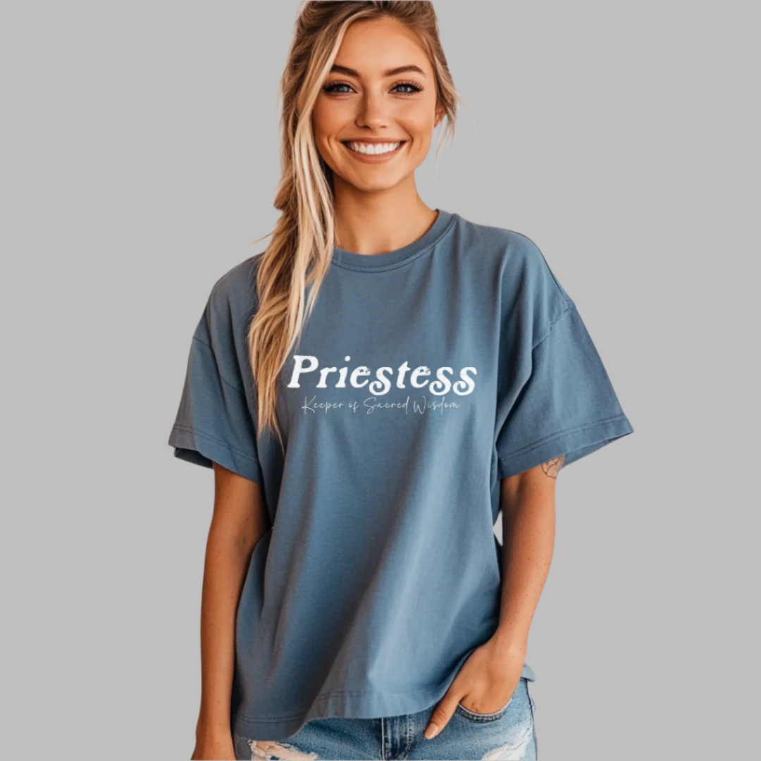 Model wearing a crew neck T-shirt. 
The shirt says “Priestess” in distressed lettering across the chest with “Keeper of Sacred Wisdom” printed in smaller scripted lettering underneath.
Wear, Embody, Be the Priestess